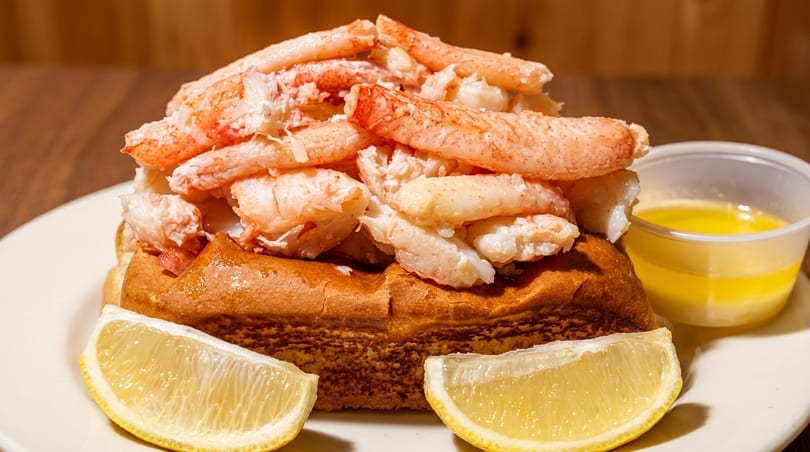A generous crab roll with lemon wedges and a side of melted butter on a white plate.