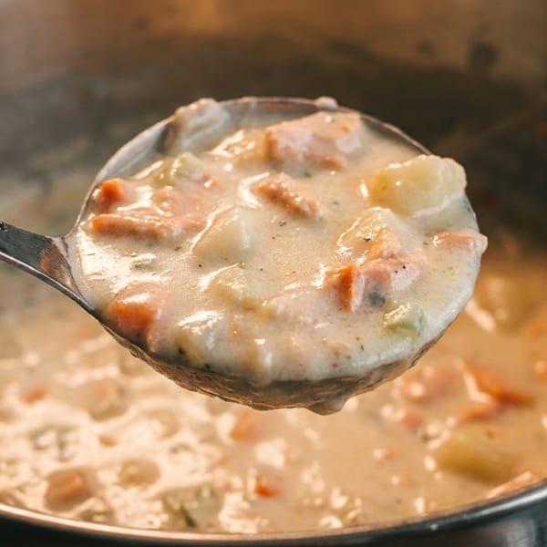 Creamy seafood chowder with potatoes, carrots, and celery being served from a large pot.
