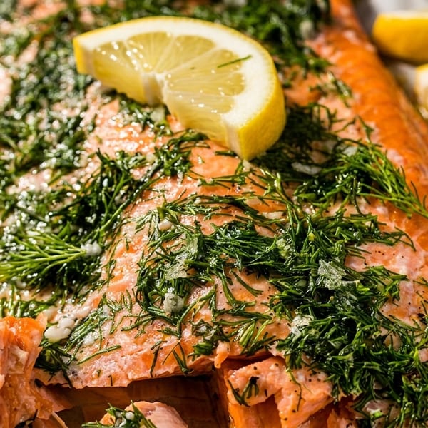 Close-up of baked salmon fillets topped with fresh dill and lemon slices.