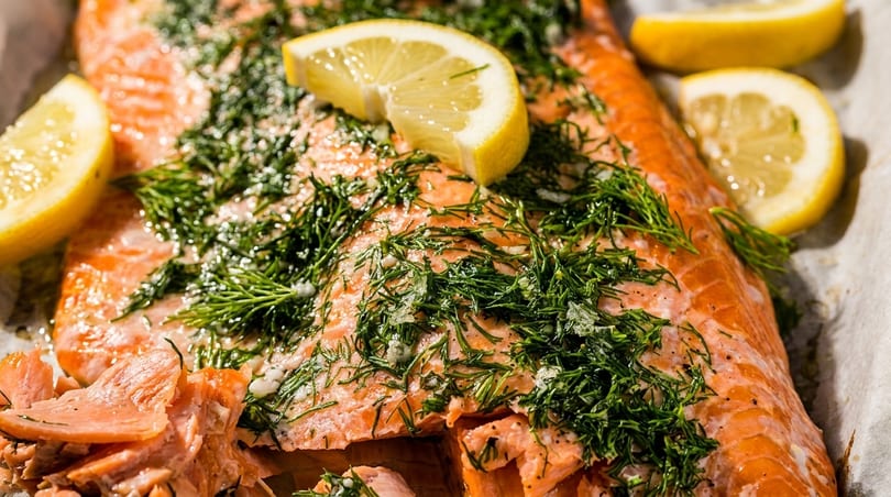 Close-up of baked salmon fillets topped with fresh dill and lemon slices.